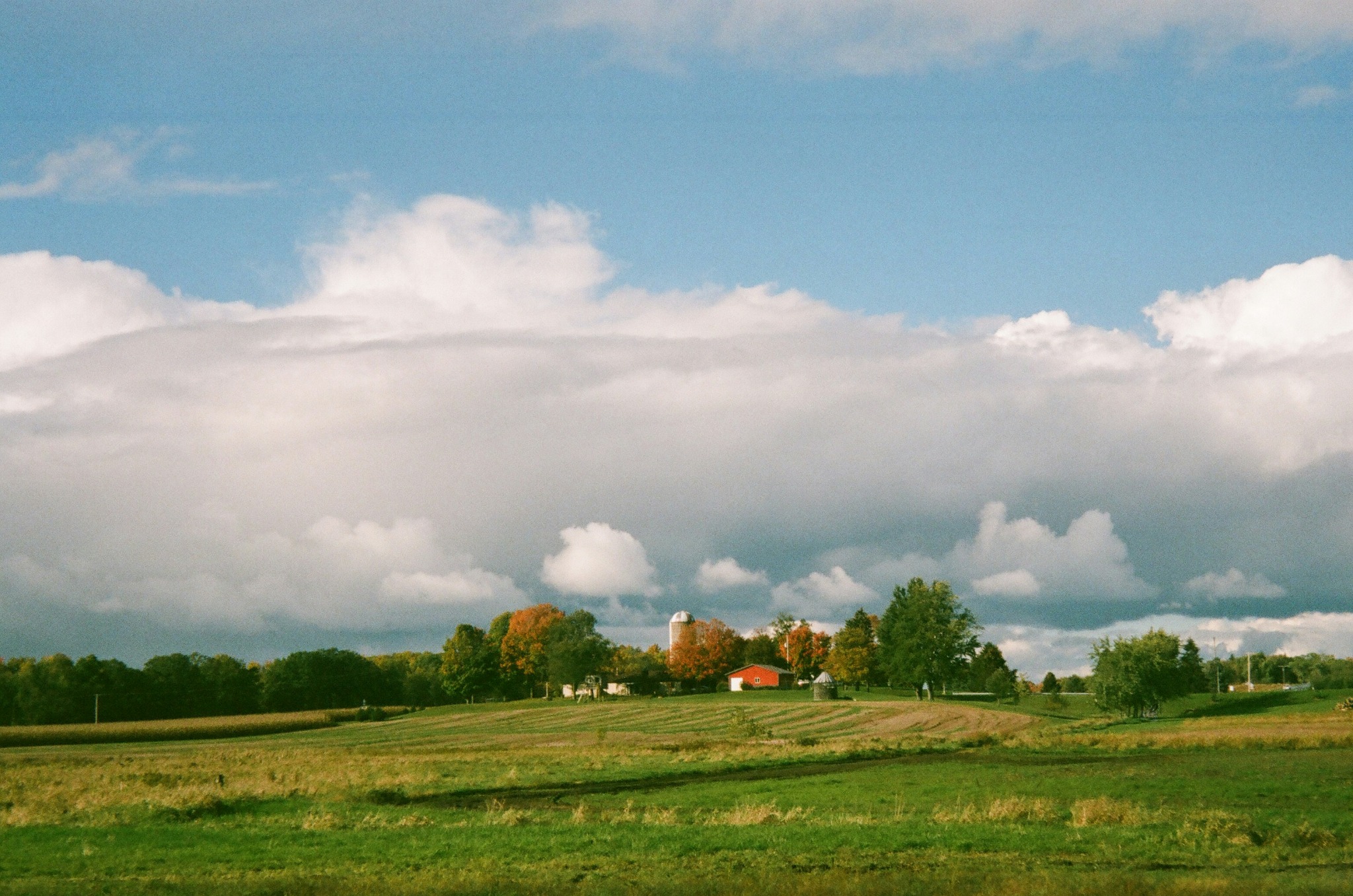 Red barn and silo beyond open fields under a cloud-filled sky