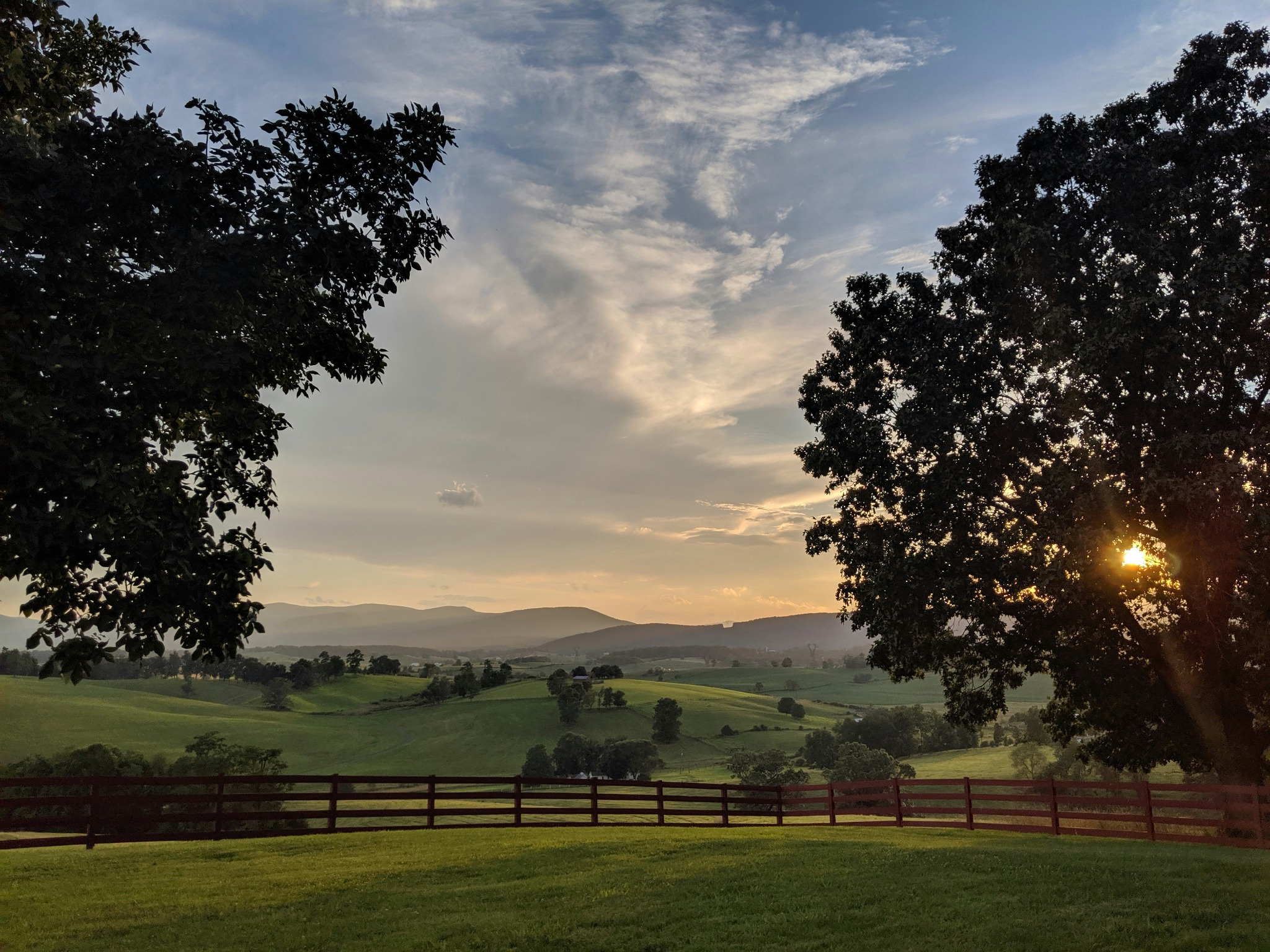 Sunset over rolling green pastures and a wooden fence